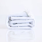 Round Boho Beach Towel by classyfashionz, rolled up in light blue with white tassels, perfect for yoga or beach use.