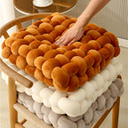 Square woven plush seat cushions in orange, cream, and gray, designed for sofas and decorative use. Soft and textured.
