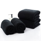 Luxury 100% Cotton Black Terry Bath & Face Towels stacked and rolled, with a soap dispenser in the center.