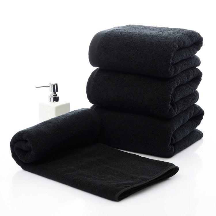 Luxury 100% Cotton Black Terry Bath & Face Towels stacked with a rolled towel and a soap dispenser beside them.