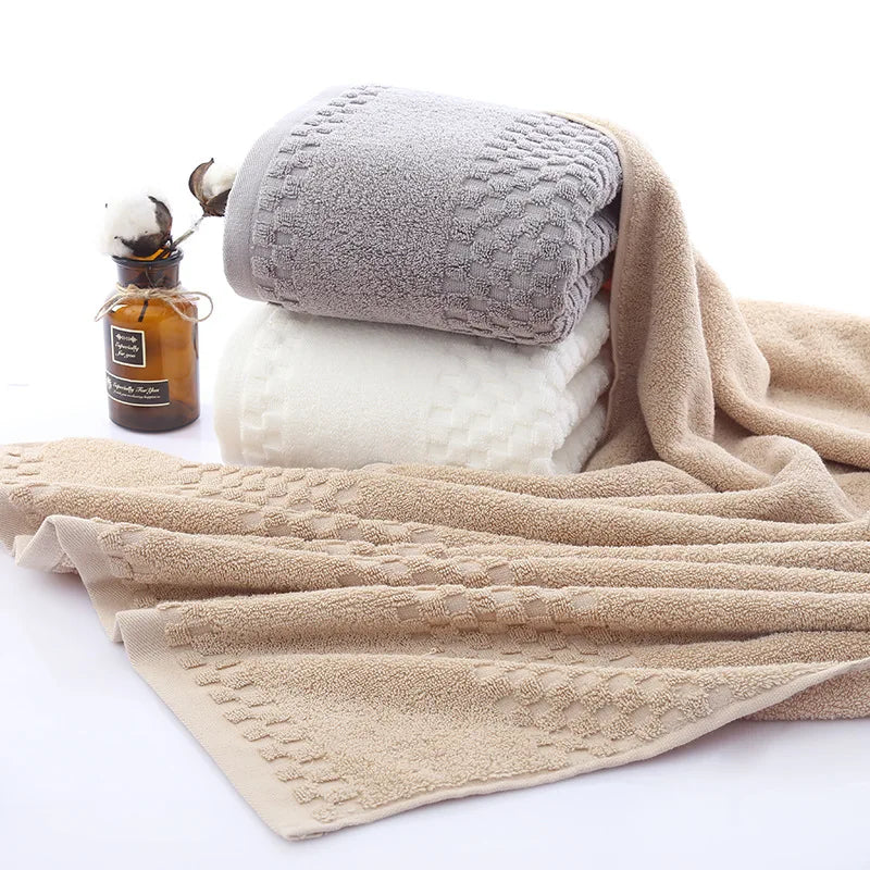 Premium Bamboo Charcoal Coral Velvet Bath Towels in gray, white, and beige stacked with a decorative bottle. Ultra-absorbent 